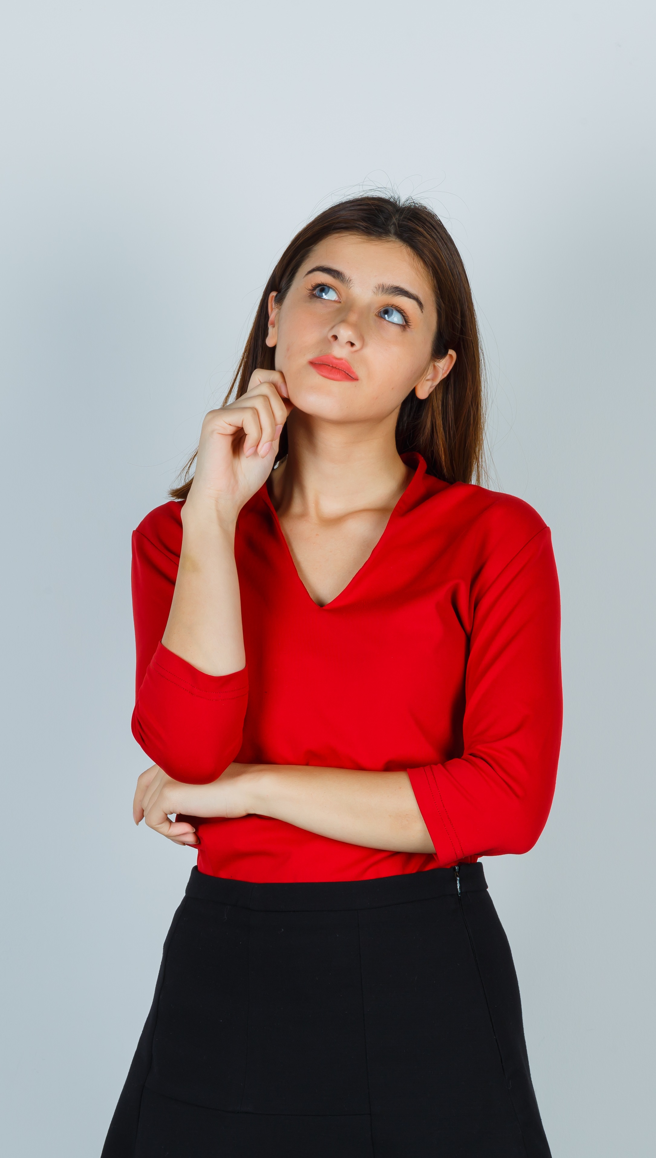 young lady in red blouse, skirt standing in thinking pose and looking pensive , front view.